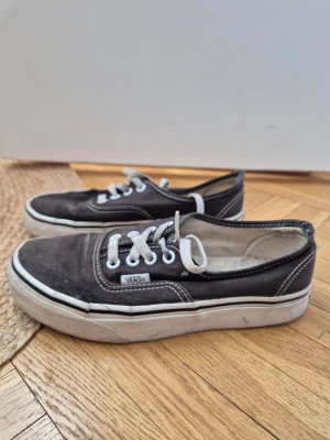 Svarta Vans Old School sneakers Stl36 - Klassiska svarta Vans Old School sneakers med vit sula och vita kontrastsömmar. Skorna har vita snören och den ikoniska Vans-loggan på sidan. Ovandelen är i canvas och sulan är i gummi med det klassiska rutmönstret undertill. Väl använda med skavanker. Återkom för detaljer!