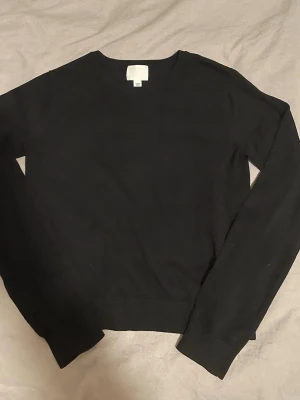 Svart basic tröja med rund hals - En stilren svart tröja med rund halsringning och långa ärmar. Perfekt att matcha med jeans eller kjol för en clean look. Tröjan har ribbade muddar vid ärmslut och nederkant. Enkel och tidlös design som passar till mycket.