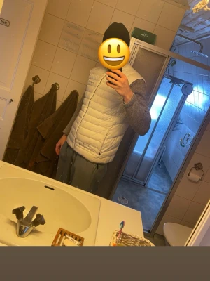 Ljusgrå dunväst från Sail Racing - Säljer en stilren ljusgrå dunväst från Sail Racing. Västen har en quiltad design, hög krage och dragkedja framtill. Perfekt att slänga över en hoodie eller tröja för extra värme. Klassisk och enkel look som funkar till det mesta.