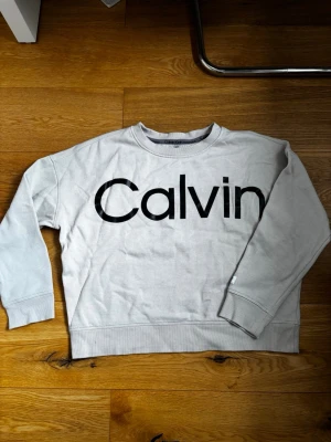 Beige tröja från Calvin Klein - Beige tröja från Calvin Klein med stor svart logga över bröstet. Storlek L men skulle säga passar M. 