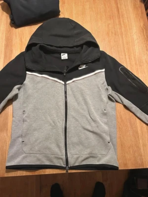 Nike mjukisbyxor svart/grå - Snygga mjukisbyxor från Nike i svart och grått med vita dragsnören och smal passform. Byxorna har ribbade muddar vid bensluten och fickor på sidorna. Perfekta för chill eller träning, tillverkade i mjukt bomullsmaterial.