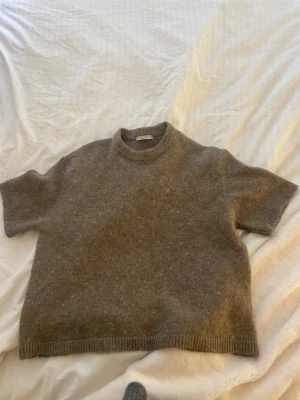 Brun stickad t-shirt i ull - Kortärmad stickad t-shirt i mjuk brun ull med rund hals och ribbade kanter. Enkel och stilren design som passar perfekt till lager på lager. Oversized passform för en avslappnad look.