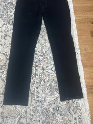 Svarta slim fit jeans från Dressmann - Svarta jeans från Dressmann i slim fit-modell. Klassisk femficksdesign och raka ben. Jeansen har diskreta sömmar och är tillverkade i ett stretchigt material för extra komfort. Perfekta för en stilren och enkel look.