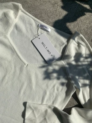 Vit långärmad topp från WOT.WOY - Stilren vit långärmad topp från WOT.WOY med mjuk och lätt ribbad struktur. Toppen har en snygg v-ringning och är tillverkad i ett stretchigt material som sitter bekvämt. Perfekt att matcha med jeans eller kjol för en enkel och fräsch look.