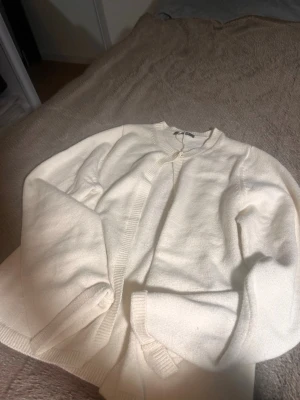 Vit ribbstickad kofta - Klassisk vit kofta med rund halsringning och ribbstickade muddar. Koftan har en enkel knapp framtill och är tillverkad i ett mjukt, stickat material. Perfekt att slänga över en t-shirt eller topp för en clean look.