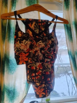 Stronger set, storlek small Calico-mönster sport-bh och leggings/tights - Träningsset från Stronger i storlek small.  Sportbh:n är v-ringad och har justerbara axelband. Leggingsen har en liten ficka bak i linningen vid ryggen. Fint mönster med ormar, fjärilar, blommor, papegojor och liljor på en svart botten. Mönstret/kollektionen heter Calico.   Leggingsens är lite slitna/noppiga på ena benet (se bild), men det syns bara när man är väldigt nära. 