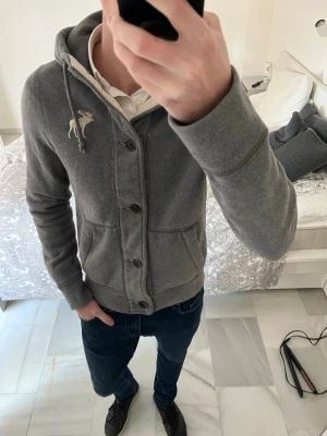 Grå Abercrombie & Fitch hoodie - Riktigt fet vintage Abercrombie & Fitch hoodie med knappar i ett fint skick 😊—————————————————————————— 📐| Storlek: M                                                          👖| Märke: Abercrombie & Fitch                            🔎 | Skick: Fint skick                                               ✍🏻 | Skriv om du har några frågor