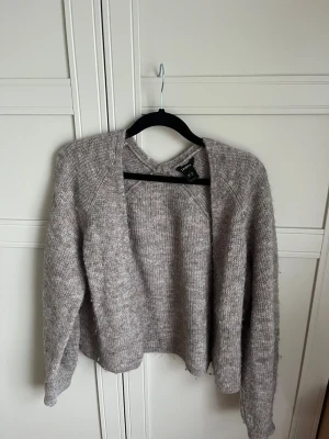 Gråmelerad stickad kofta H&M - Mysig gråmelerad stickad kofta från H&M med öppen front och avslappnad passform. Koftan har långa ärmar och är tillverkad i ett mjukt, fluffigt material som passar perfekt för kyliga dagar. Enkel att matcha med olika outfits.