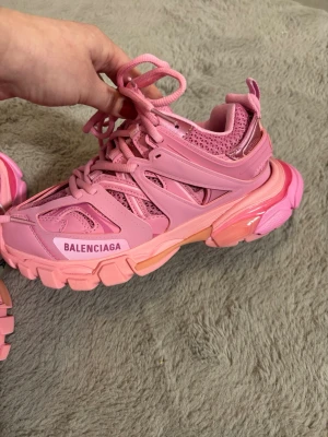  rosa sneakers - Säljer ett par chunky rosa Balenciaga sneakers med mesh och syntetdetaljer. Skorna har kraftig sula, flera lager och coola snörningar. Märket syns tydligt på sidan och tungan. Perfekta för dig som vill sticka ut med färg och design.