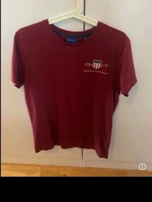 Vinröd t-shirt från Gant - Snygg vinröd t-shirt från Gant med tryckt logga och emblem på bröstet. Klassisk rund halsringning och korta ärmar. Tillverkad i mjuk bomull som känns skön mot huden. Perfekt för en avslappnad och stilren look.