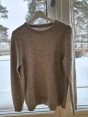 Beige stickad tröja med rund hals - En stilren beige stickad tröja med rund halsringning och ribbade muddar vid ärmslut och nederkant. Tröjan har en klassisk passform. Tröjan är från These glory Days. Tröjan har jag själv köpt på Plick då i nytt skick sedan har jag använt den 1 gång. Själv har jag aldrig tvättat den.