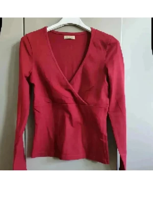 Röd omlottopp från Only - Snygg röd omlottopp från Only med v-ringning och långa ärmar. Toppen har en figurnära passform och är tillverkad i mjukt bomullsmaterial. Perfekt att styla med jeans eller kjol för en trendig look.
