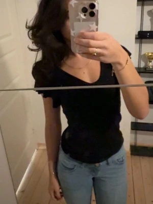 Svart v-ringad topp - Snygg svart topp med v-ringning och korta volang ärmar. Enkel och stilren design som passar till mycket. Perfekt att matcha med jeans eller kjol för en trendig look.