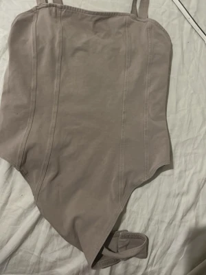 Beige body med smala axelband - Stilren beige body med smala axelband och markerade sömmar framtill. Tillverkad i mjukt stretchigt material som sitter skönt mot kroppen. Perfekt att styla med jeans eller kjol för en clean look.