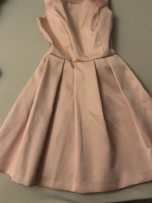 Ljusrosa kort klänning med rosetter - Supersöt ljusrosa klänning med utställd kjol och två dekorativa rosetter i ryggen. Klänningen är ärmlös och har en feminin, elegant siluett som passar perfekt till sommarens alla tillfällen. Tillverkad i ett mjukt tyg som ger en skön känsla.