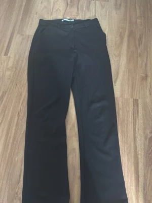 Svarta kostymbyxor från lager 157 - Stilrena svarta kostymbyxor  med raka ben och klassisk passform. Byxorna har hällor för skärp och stängs med knapp och dragkedja. Perfekta för en clean och snygg look. Materialet känns mjukt och följsamt.