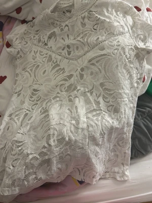 Vit spetsblus med kort ärm - Säljer en vit blus med kort ärm och vackert spetsmönster. Toppen har en rund halsringning och ett tunt innerfoder för extra komfort. Perfekt för dig som gillar romantiska detaljer och stilren look.