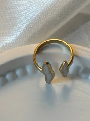 Ett guldpläterad ring  - Ett guldpläterad ring med vita detaljer på ringen. Perfekt för dig som gillar unika accessoarer med en touch av elegans.