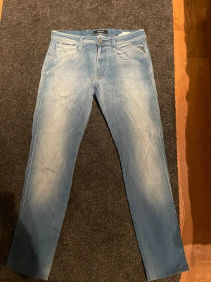 Ljusblå jeans från Replay - Säljer ett par ljusblå jeans från Replay med klassisk femficksmodell och snygga slitningar framtill. Jeansen har raka ben och normal midja. Perfekta för dig som gillar en avslappnad men trendig stil.