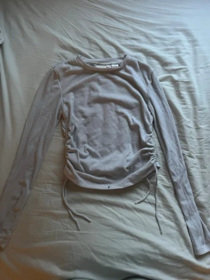 Vit ribbad långärmad topp - Trendig vit ribbad topp med långa ärmar och snörning i sidorna för en snygg passform. Perfekt att styla med jeans eller kjol för en cool vardagslook. Storlek 158-164 men passar som ungefär XXS.