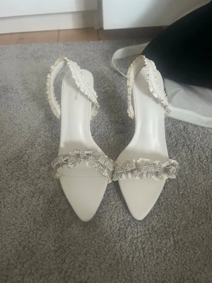 Vita högklackar med silvriga rosor Prettylittlething  - Aldrig använda, endast testade. Ganska hög klack