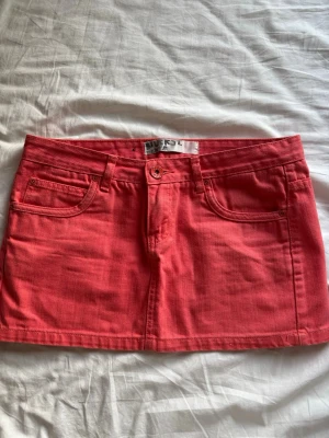 Rosa jeanskjol  - Snygg aprikos röd/rosa jeanskjol från dvrs med klassisk femficksdesign och knappstängning fram. 