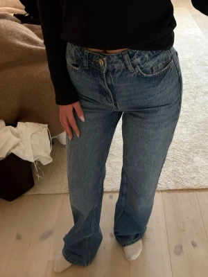 Blå raka jeans med hög midja - Säljer ett par klassiska blå jeans med rak passform och hög midja. Jeansen har fem fickor, bälteshällor och stängs med knapp och dragkedja. Perfekta till en avslappnad stil och passar till det mesta. Materialet är kraftig denim i bomull.