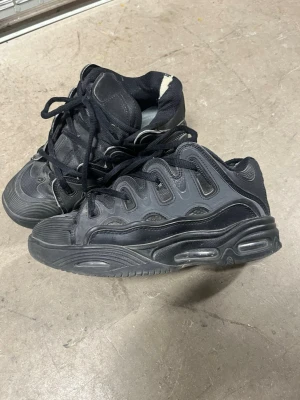 Osiris D3 svart - Säljer ett par svarta Osiris d3 sneakers med kraftig, chunky sula och luftbubblor. Skorna har detaljer i syntetmaterial och mesh, samt svarta skosnören. Perfekt för dig som gillar en sportig och modern look. Allt i pm