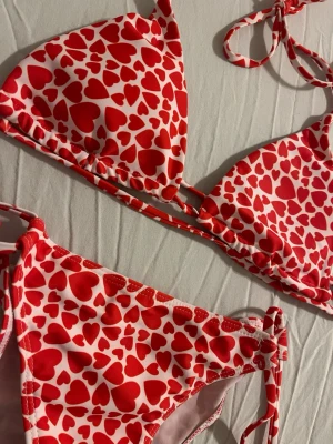 NY! Röd bikini set med hjärtan - NY! Supersöt bikini med rött hjärtmönster. Klassisk trekantsmodell med knyt både i ryggen och på sidorna av bikinitrosan. 