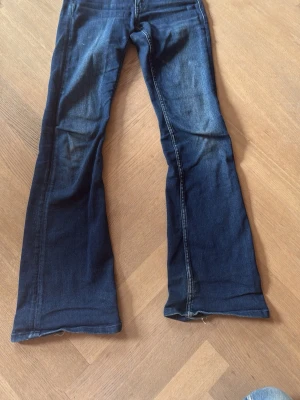 Blå bootcut jeans från Gina Tricot - Säljer ett par mörkblå bootcut jeans från Gina Tricot med dubbla knappar framtill. Jeansen har klassisk femficksdesign och är tillverkade i stretchigt denimtyg. Perfekta för dig som gillar en retroinspirerad look med utsvängda ben.