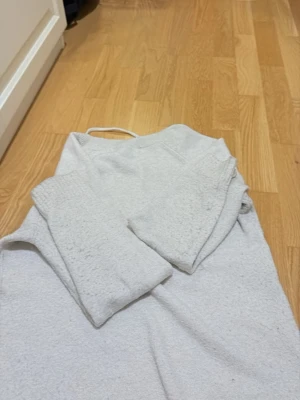 Ljusgrå stickad tröja - En enkel och stilren ljusgrå stickad tröja med rund hals och långa ärmar. Tröjan har ribbstickade muddar vid ärmslut och nederkant. Perfekt basplagg för lager på lager och passar till det mesta.