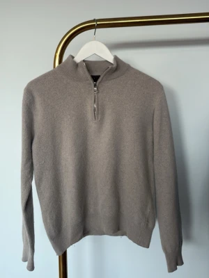 Beige halvzip tröja Oscar Jacobson - Säljer en beige stickad tröja från Oscar Jacobson med halv dragkedja och hög krage. Tillverkad i Italien, mjukt material och ribbade muddar vid ärmslut och nederkant. Perfekt för lager på lager och stilren look. Den är lite kort i längden så va beredd på att ärmarna sitter normalt men att den kan va lite kort i midjan.