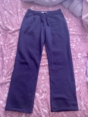 Mörkblå mjukisbyxor från 157 - Mörkblå mjukisbyxor från 157 med raka ben och dragsko i midjan. Byxorna har resår i midjan och är gjorda i ett mjukt, fleeceliknande material på insidan. Perfekta för en chill dag hemma eller när du vill vara extra bekväm.