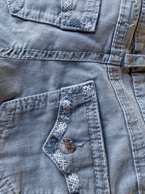 Grå jeans med broderade detaljer - Snygga grå jeans från Gina Tricot med unika broderade detaljer på fickorna och coola silverknappar med blom-motiv. Jeansen har klassisk femficksdesign och är tillverkade i mjukt denim-material. Perfekt för dig som vill ha något extra i garderoben. De är low Waist i storlek 158 har aldrig användts köpta för 300 och säljer för 100 kan tänka mig att sänka mitt pris så kontakta isåfall💕