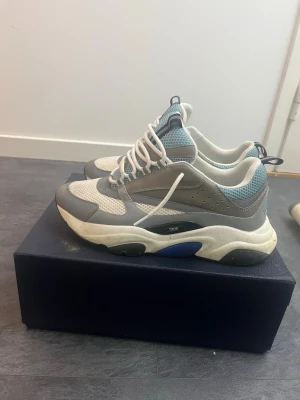 Grå och vita chunky sneakers - Chunky sneakers i grått, vitt och blått med meshdetaljer och tjock sula. Skorna har snörning och sportig design med ventilerande material och kontrastfärgade partier. Perfekta för dig som gillar streetwear och en modern look.