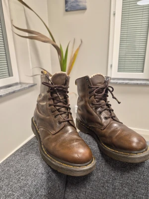 Dr. Martens 1460 Serena Kängor Bruna Storlek 39 - Säljer ett par bruna Dr. Martens stövletter i läder med snörning och gul söm runt sulan. Insidan är fodrad med mjukt foder för extra värme. Klassisk chunky sula och dragflik bak. Perfekta för dig som vill ha en cool och tidlös look.