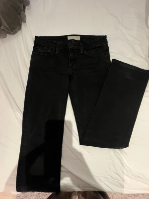 Svarta bootcut jeans  - Säljer ett par svarta bootcut jeans från Marc Jacobs i storlek 26. Jeansen har klassisk femficksdesign, låg midja och tydliga M-detaljer på bakfickan.