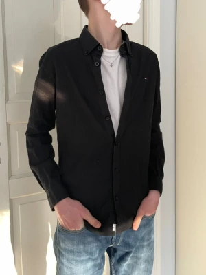 Tommy Hilfiger Skjorta  - Svart Tommy Hilfiger skjorta. Modellen är 173 cm, skjortan är storlek 164, den sitter ungefär som en Small. En skjorta i mycket bra skick som blir riktigt snyggt till både fest och vardagen Skriv gärna om ni har fler frågor!😁 Pris kan diskuteras👍