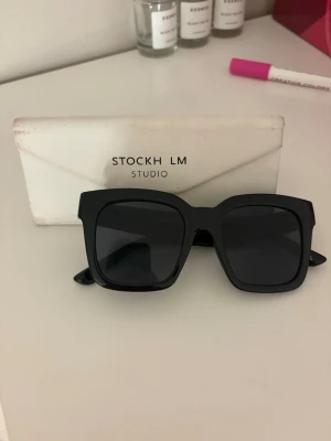 Svarta solglasögon  - Säljer ett par svarta solglasögon från Stockh LM studio. De har en fyrkantig form som passar dig som gillar lite större glasögon. Perfekt inför våren och sommaren nu när solen har kommit fram. 