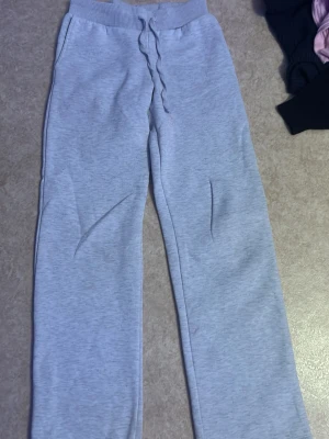 Ljusgrå mjukisbyxor med dragsko - Säljer ett par ljusgrå mjukisbyxor med bred resår i midjan och dragsko för skön passform. Byxorna har raka ben och sidofickor. Perfekta för chill dagar eller när du vill vara extra bekväm. Materialet känns mjukt och stretchigt.