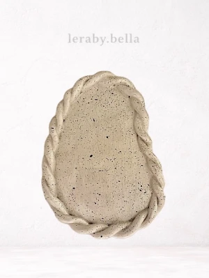 Handgjord beige fat - Unikt handgjort fat i lera med oregelbunden oval form och flätad kant. Ytan har små svarta prickar som ger en rustik känsla. Perfekt som dekoration eller för servering av småsaker.