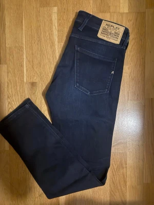 Replay Anbass mörkblå 30/32 - Snygga mörkblå jeans från Replay med klassisk femficksdesign och raka ben. Jeansen har en stilren look med läderpatch bak i midjan och diskreta sömmar. Perfekta för dig som gillar en clean och tidlös stil.