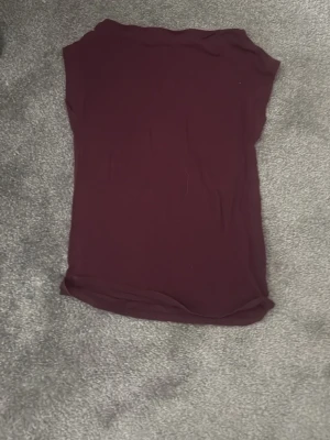 Vinröd ärmlös topp - En enkel och stilren vinröd topp utan ärmar. Toppen har en rak passform och är tillverkad i ett mjukt, stretchigt material som känns skönt mot huden. Perfekt att matcha med jeans eller kjol för en clean look.