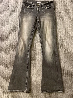 Grå bootcut jeans med kontrastsömmar🦋 - Säljer ett par grå bootcut jeans med snygga slitningar och kontrastsömmar. Jeansen har dubbla knappar i midjan, framfickor med lock och dekorativa bakfickor med broderade fickor🤩