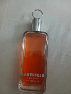 Lagerfeld Classic Eau de Toilette - Lagerfeld Classic Eau de Toilette med en rektangulär glasflaska och metallock. Parfymen har en varm orange färg och flaskan har en stilren design med tydlig logotyp.Huvud noterna är bergamott, citrus och muskatellsalvia. Mitt noterna är tobak, ros och cederträ basnoten är vanilj, tonka böna och musk. 
