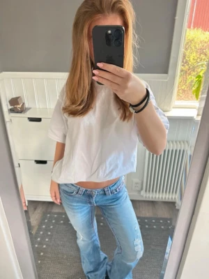 Ljusblå bootcut jeans med brodyr - Säljer ett par ljusblå bootcut jeans med snygg slitning och rosa broderade detaljer på bakfickorna. Jeansen har låg midja och klassisk femficksdesign. Perfekta för en avslappnad och trendig look.