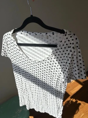 Vit prickig t-shirt från 157 - Säljer en vit t-shirt från 157 med svarta prickar över hela plagget. T-shirten har korta ärmar och en klassisk rund halsringning. Tillverkad i mjuk bomull som känns skön mot huden. Perfekt för dig som gillar en lekfull och trendig stil🥂