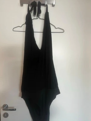 Svart djup urringad body - Stilren svart body med djup urringning och tunna axelband. Tillverkad i mjukt, stretchigt material som formar sig efter kroppen. Perfekt för dig som gillar minimalistisk och trendig stil. Inga synliga detaljer eller mönster. Rök och djurfritt hem. Pruta gärna 🌸