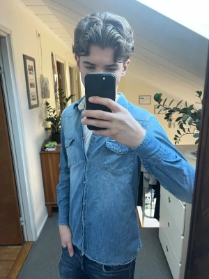 Ljusblå jeansskjorta från Dondup - Säljer en ljusblå jeansskjorta i bomull från Dondup. Skjortan har klassisk krage, bröstfickor med knapp och knappar längs hela framsidan. Perfekt till jeans för en avslappnad look.