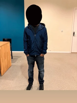  Moncler windbreaker - Snygg mörkblå vindjacka från Moncler med huva och dragkedja framtill. Jackan har Moncler-logga på ärmen och diskreta rödvita detaljer vid huvan. Tillverkad i ett glansigt, lätt material som passar perfekt för blåsiga dagar.